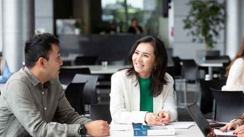 Two older postgraduate students sitting at a table and talking to one another